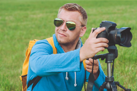 Young handsome happy man smiling with a camera in his hands. against the background of green grassの写真素材