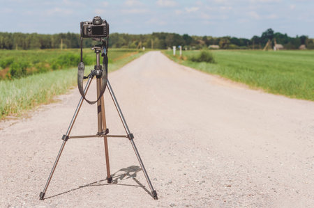 professional photo video camera on a tripod. Background of the road in the field with blue skyの写真素材