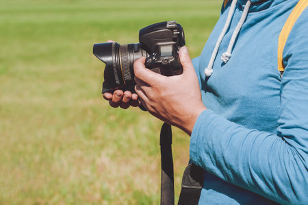Professional camera in the hands of a man. Against the backdrop of a green lawnの写真素材