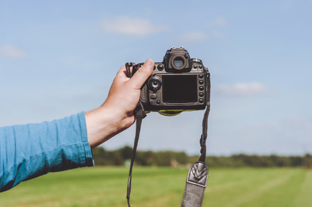 The camera is in the hand of a guy. Against the background of the sky and grassの写真素材