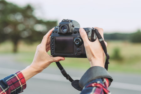 Professional camera in the hands of a girl. Background trees field and road