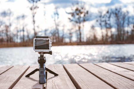 Mockup action camera stands on a pier near a river or lake. Sky background with treesの写真素材