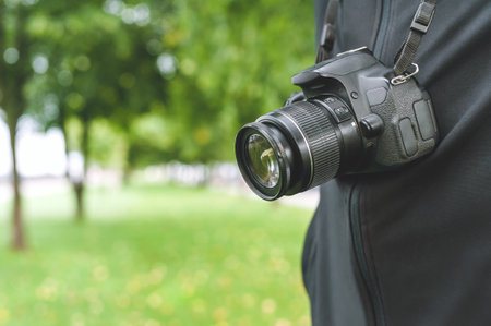 Close-up, a photo-video camera hangs on a man. Against the backdrop of a beautiful park with trees and a lawn. Vacation time in natureの写真素材