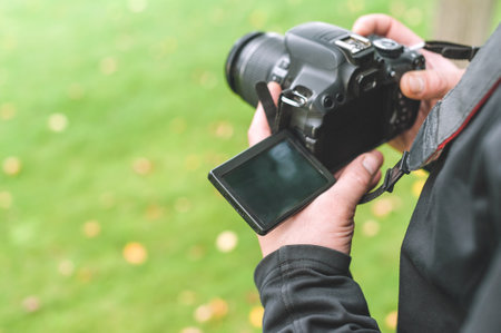Close-up, a model of a professional digital camera is held by a man in his hands. Green grass...