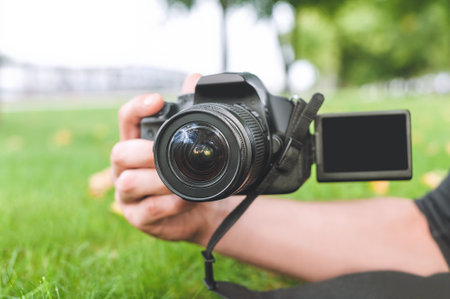 Close-up, photo-video camera in a man's hand. background of grass and trees in the park on the lawnの写真素材