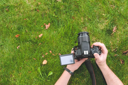 Professional camera in the hands of a man. Green grass background with yellow leaves. Top view