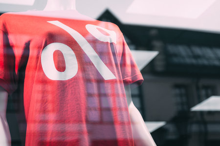 Close-up of a red T-shirt with a large white percent symbol on a mannequin in a store window, indicating a sale or special offer. The glass shows reflections of the outside environment.の写真素材