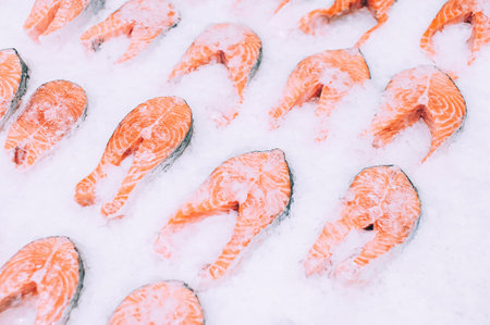 A close-up view showcases numerous fresh salmon fillets with their characteristic pink flesh, arranged on a bed of crushed ice to maintain their freshness for purchase.の写真素材
