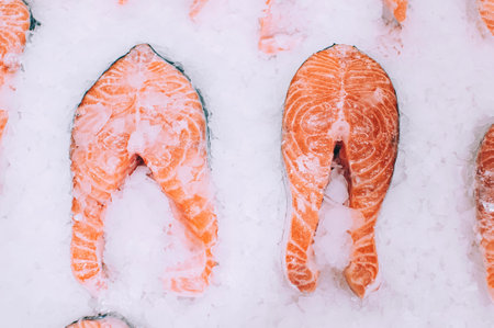 The image focuses on two fresh salmon tail pieces, showing their distinct bone structure and pink flesh, presented on a bed of crushed ice at a fish market or store.の写真素材