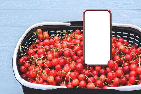 Close-up mockup of a smartphone in a basket with ripe red cherries. On a gray backgroundの写真素材