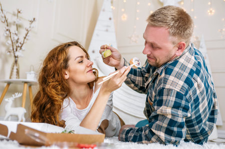 A man and a woman eat sushi lying on the floor in the house.の写真素材