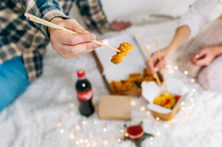 A man and a woman eat breaded shrimp nuggets from a take-out box. Topic: fast food home delivery. Back viewの写真素材