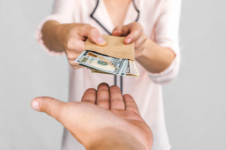 A woman passes money dollars from a paper bag into a man's hand. On a white background