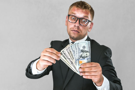 Businessman with emotional wild look on his face. Holds American dollars in his hands on a gray and white backgroundの写真素材