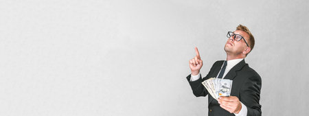 Banner, Businessman in a suit shows thumbs up and holds american dollars in his hands on a...