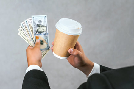 Close-up of American money with a disposable glass of takeaway coffee in the hands of a businessman...