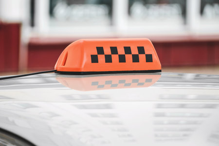 An orange taxi sign with a checkered pattern on a car roof, reflecting on a glossy surface. Blurred urban background with buildings adds a city vibe.の写真素材