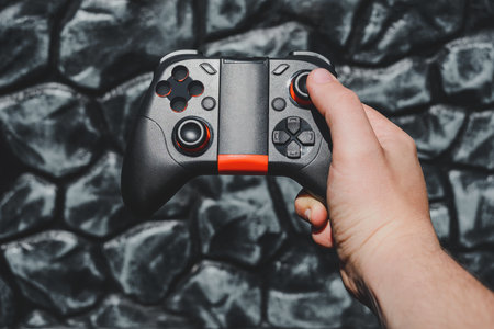 A hand hold a sleek black and orange mobile gaming controller against a textured dark background, showcasing portable gaming technology and interactive entertainment.の写真素材
