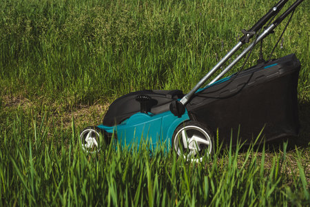 Modern electric lawn mower in action, trimming tall green grass in a garden. Eco-friendly gardening...