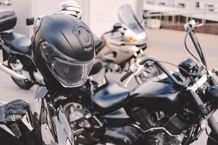 A sleek black motorcycle helmet rests securely on the handlebars of a parked motorcycle, with other bikes blurred in the background, signaling adventure, freedom, and the open road.の写真素材