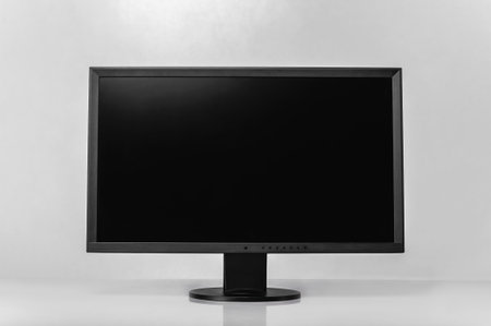 A sleek black monitor display sits on a white desk, perfect for office or home use. The modern design and clean background make it ideal for tech setups.の写真素材