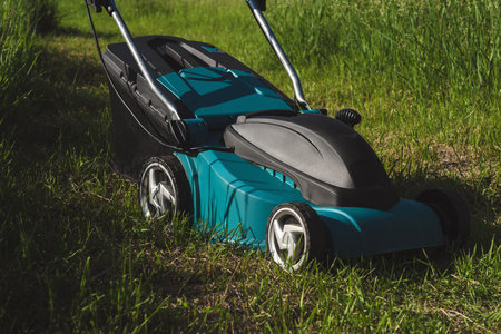 Electric lawn mower standing on lush green grass in a sunny garden. Modern gardening tool for...