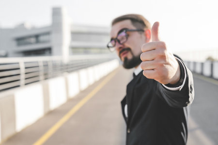 A blurred man in glasses and a suit gives a confident thumbs-up gesture against a sunny, bright...