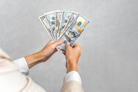 Two hands carefully display a fan of various US dollar banknotes (1, 5, 10, 20, 50, 100),...