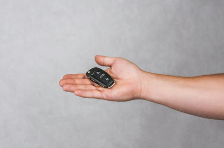 An open hand presents a modern black car key remote, highlighting vehicle security systems and peace...