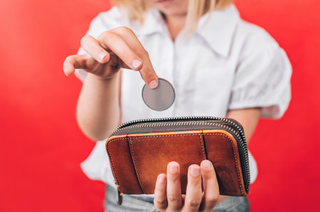 A child's hands are shown, one dropping a coin into a brown leather wallet held by the other hand, illustrating concepts of saving and early financial education.の写真素材