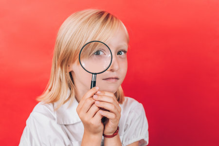 A young child holds a magnifying glass close to their face, looking through it with curiosity, symbolizing exploration and the search for a future profession or interests.の写真素材