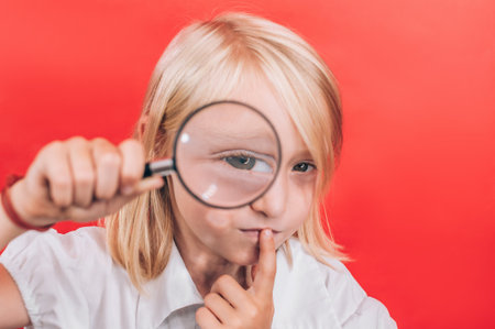 A young girl intently looks through a magnifying glass while touching her lips, symbolizing thoughtful consideration and the important choice of a future profession.の写真素材