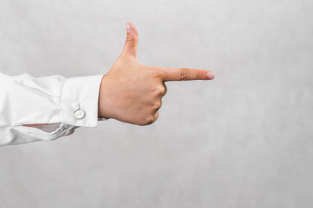 A hand in a white shirt sleeve points right with an extended index finger, symbolizing guidance, direction, or instruction against a neutral gray background.の写真素材