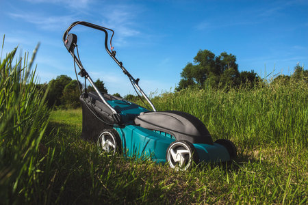 A modern electric lawn mower stands on a bright green field under a clear blue sky, ideal for summer...