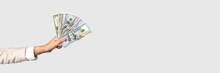 Wide banner image featuring a hand holding various US dollar banknotes, perfect for finance...