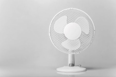A small, modern white table fan with a protective mesh and three blades stands on a reflective surface.の写真素材