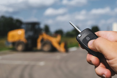 A close-up of a man opening a construction vehicle with a key fob, with a yellow forklift parked in a parking lot in the backgroundの写真素材