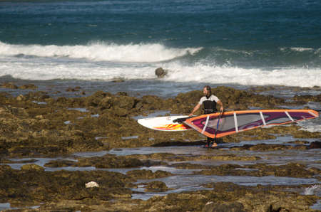 Aguimes. Gran Canaria. Canary Islands. Spain. March 25, 2014: windsurfer carrying his windsurf board in Arinaga.のeditorial素材