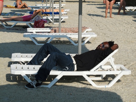 a black african resting after night working as dancer in night club at ukrainian sea beachのeditorial素材