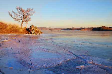 Lake Baikal in December. View of the frozen Kurkut Bay in the rays of the setting sun. Larch on the...