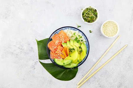 Poke bowl with salmon, rice, avocado, cucumber, mango, micro green and carrot. Hawaiian diet food with fish. Top view. Flat lay.の写真素材