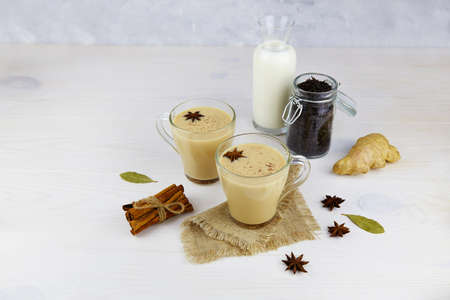Traditional masala chai in cup with ingredients for making tea on a gray background.