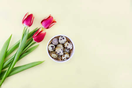 Natural quail eggs in a ceramic bowl and bright tulips on a yellow background. Easter holiday. Spring greeting card.の写真素材