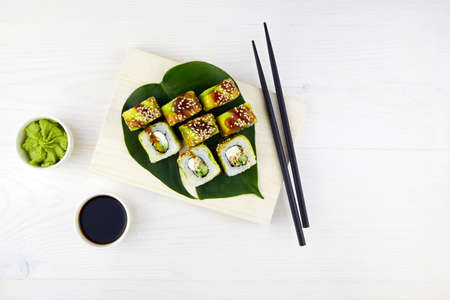 Sushi set on wooden background. Sushi roll Maki with filling of cream cheese, smoked eel, cucumber, wrapped in slices from avocado, poured with unagi sauce.の写真素材