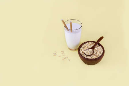 Oat milk in a glass, oat flakes in a ceramic bowl on a yellow background. Vegetable milk, vegan lactose free. Copy space.の写真素材