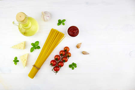 Ingredients for making pasta: linguini, tomato, sauce, basil, cheese on a white wooden background. Top view.の写真素材