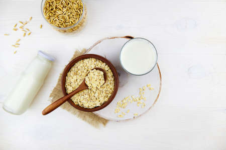 Oatmeal milk in a glass and a bottle, oatmeal flakes in a ceramic bowl on a white wooden background. Vegetable milk. Vegan lactose free. Top viewの写真素材