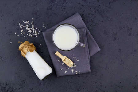 Rice milk in a glass mug and a bottle on a dark gray background. Vegetable milk. Vegan lactose free. Top view, copy space.の写真素材