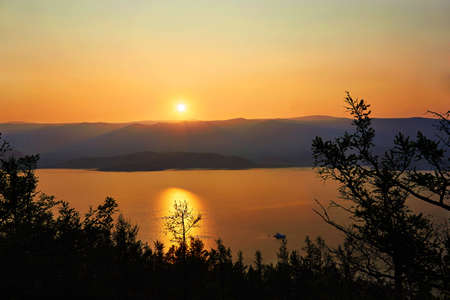 Beautiful orange sunset over the mountains in summer. The rays of the setting sun are reflected in...