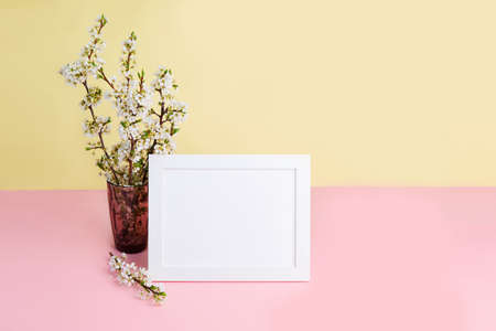 A bouquet of flowering plum branches in a vase and a photo frame with space for text. Spring holiday...